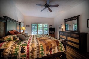 A bedroom with a large bed, a ceiling fan, a dresser, a television, and a window with a view of trees. - Cozy Family Mountain Home in Seven Springs (CHAMPION)