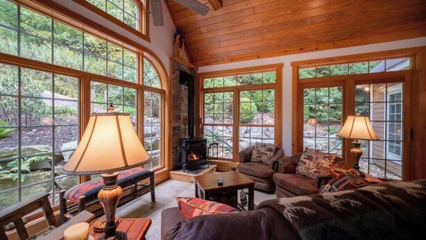A cozy cabin interior with large windows, a fireplace, and wooden furnishings. - Cozy Family Mountain Home in Seven Springs (CHAMPION)
