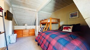 A cozy attic bedroom with a bunk bed, a dresser, a TV, and a large window. - Rustic Mountain Cabin, Outdoor Pool & Hot Tub On-site. Golf Course Nearby! (Mammoth Lakes)