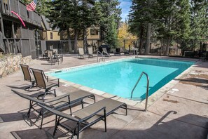 A swimming pool with lounge chairs and a barbecue area, surrounded by trees and a fence. - Rustic Mountain Cabin, Outdoor Pool & Hot Tub On-site. Golf Course Nearby! (Mammoth Lakes)