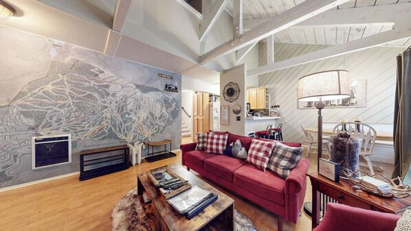 A living room with a large map on the wall, a red sofa, a wooden coffee table, and a lamp. - Rustic Mountain Cabin, Outdoor Pool & Hot Tub On-site. Golf Course Nearby! (Mammoth Lakes)