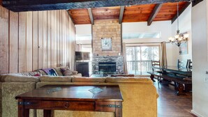 Un salón acogedor con chimenea de piedra, vigas de madera en el techo y un amplio ventanal con vistas a un paisaje nevado.