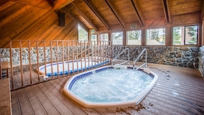 Ein Innenbereich mit Whirlpool, Holzterrasse, Steinwänden und einer Steintreppe, die zu einer erhöhten Ebene führt.