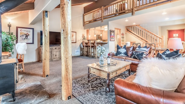Ein geräumiges Wohnzimmer mit hoher Decke, Holzbalken, einer Treppe und einer gemütlichen Sitzecke mit Ledersofa und Couchtisch.