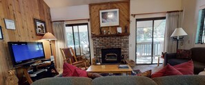 Cozy living room with a fireplace, comfortable seating, and a television, offering a view of the outdoors.