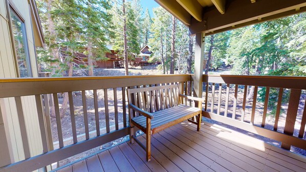 Relax on the deck with a bench, surrounded by a railing, and take in the serene views of the forest and nearby cabin.