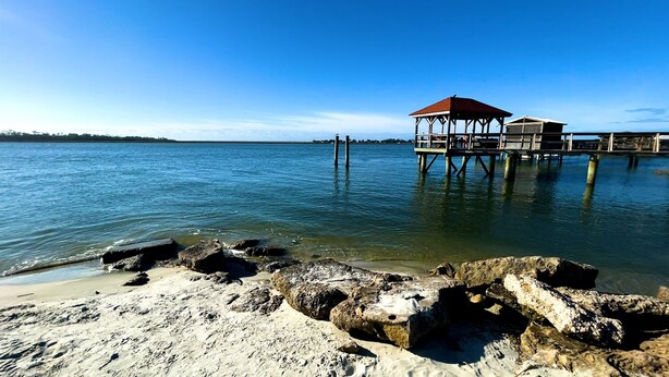 A pier extending into calm water with a covered structure at the end. - Beautiful home with pool. See notes about heated pool season. (Tybee Island)