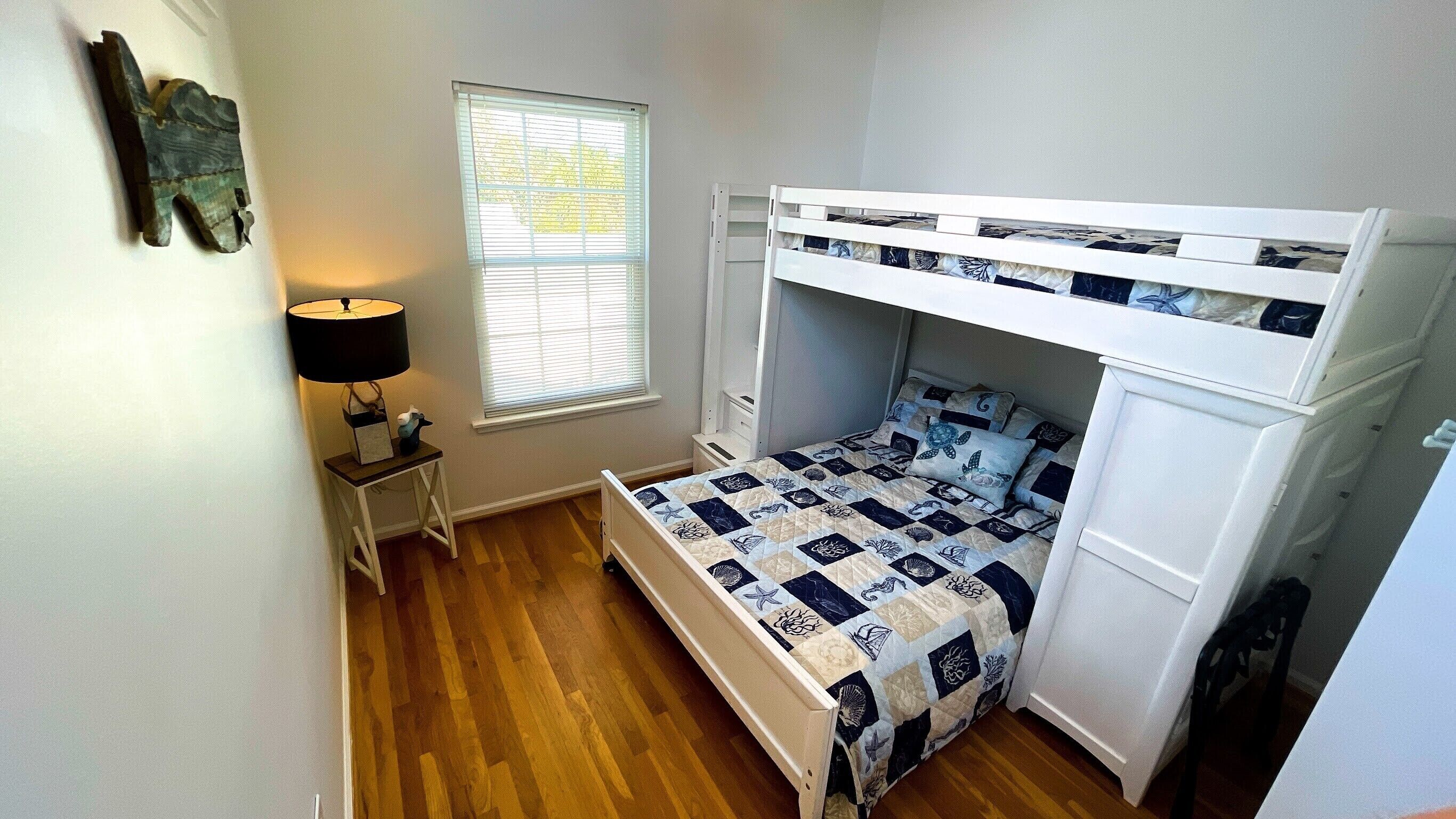 A compact bedroom with a bunk bed, a bedside table with a lamp, and a window with blinds.