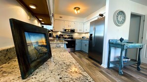 A modern kitchen with granite countertops, stainless steel appliances, and light blue cabinets. - Beautiful home with pool. See notes about heated pool season. (Tybee Island)