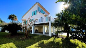 A two-story house with a covered porch, a lawn, and surrounding greenery. - Beautiful home with pool. See notes about heated pool season. (Tybee Island)