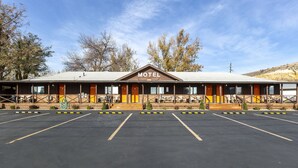A motel with a central entrance, multiple rooms with wooden doors, and a parking lot. - Weiser Motel & RV Park (Weiser)
