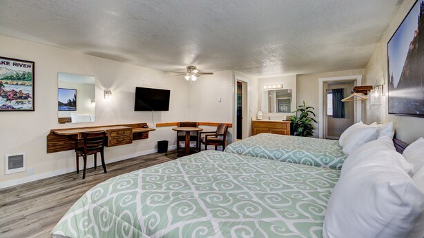 A hotel room with two beds, a desk with a chair, a television, and a bathroom with a mirror and lights. - Weiser Motel & RV Park (Weiser)