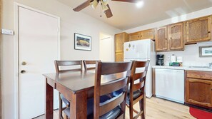 A compact kitchen with wooden cabinets, a white refrigerator, and a dining area with a wooden table and chairs.