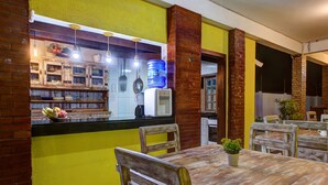 A kitchen with a yellow wall, wooden chairs, a table with a plant, and a water dispenser. - Casa 25pessoas c piscina Porto das Dunas (Aquiraz)