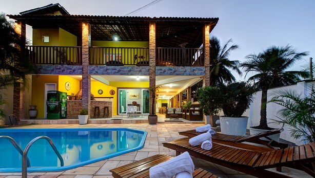 A two-story house with a swimming pool, lounge chairs, and a patio area. - Casa 25pessoas c piscina Porto das Dunas (Aquiraz)