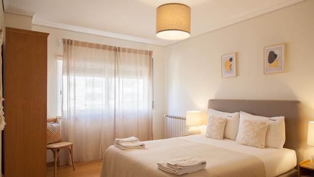 A neatly arranged bedroom with a large bed, a chair, and a desk. - FLH Cascais Wooden Spacious Apartment (Cascais)