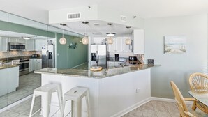 Una cucina moderna con isola centrale, mobili bianchi, elettrodomestici in acciaio inossidabile e zona pranzo con sedie in vimini.