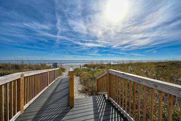 A wooden boardwalk leading to a beach with a clear sky.