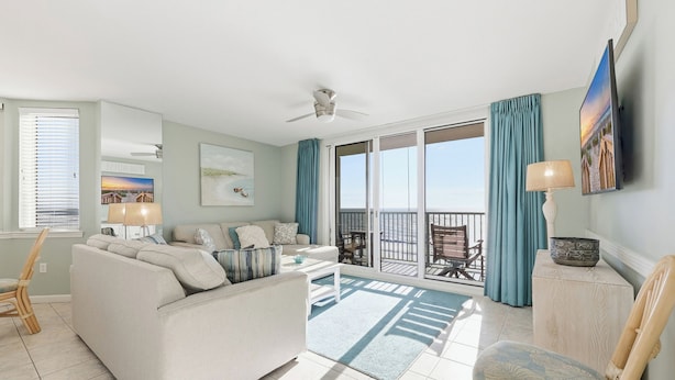 A spacious living room with a large sofa, a coffee table, and a balcony with a view.