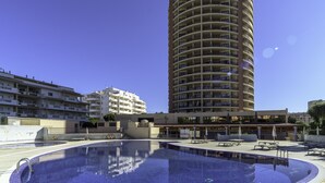 A hotel with a swimming pool, multiple balconies, and a clear blue sky.