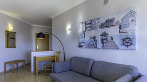 A living room with a gray sofa, a wooden desk, a chair, a small table, and a wall with nautical-themed artwork.
