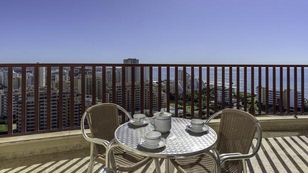A balcony with a table set for tea, overlooking a cityscape and the sea.