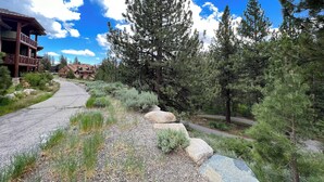 A lodge with a stone pathway leading to a wooden building, surrounded by dense pine trees and a clear blue sky. - Modern Home, Great Mountain Views, Private Hot Tub, Gas Grill & Washer/Dryer (Mammoth Lakes)