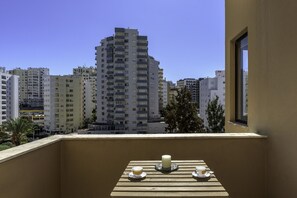 A balcony with a table set for two, overlooking a cityscape with high-rise buildings. - FLH Praia da Rocha Marine Design Flat (Portimão)