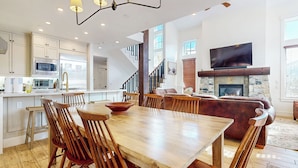 A spacious living area with a large wooden dining table, comfortable seating, a fireplace, and a kitchen with modern appliances. - Remodeled & Beautiful Home. Private Hot Tub & Gas Grill, Near Biking Trails (Mammoth Lakes)