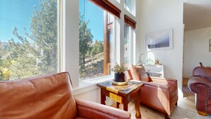 A room with leather chairs, a wooden table, and a view of trees through large windows. - Remodeled & Beautiful Home. Private Hot Tub & Gas Grill, Near Biking Trails (Mammoth Lakes)