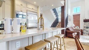 A modern kitchen with a central island, stainless steel appliances, and a wooden bar stool seating area. - Remodeled & Beautiful Home. Private Hot Tub & Gas Grill, Near Biking Trails (Mammoth Lakes)