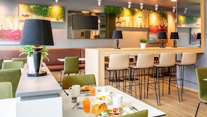 Un espace repas moderne avec une longue table dressée pour le petit-déjeuner, des tabourets de bar et un coin salon avec un canapé.