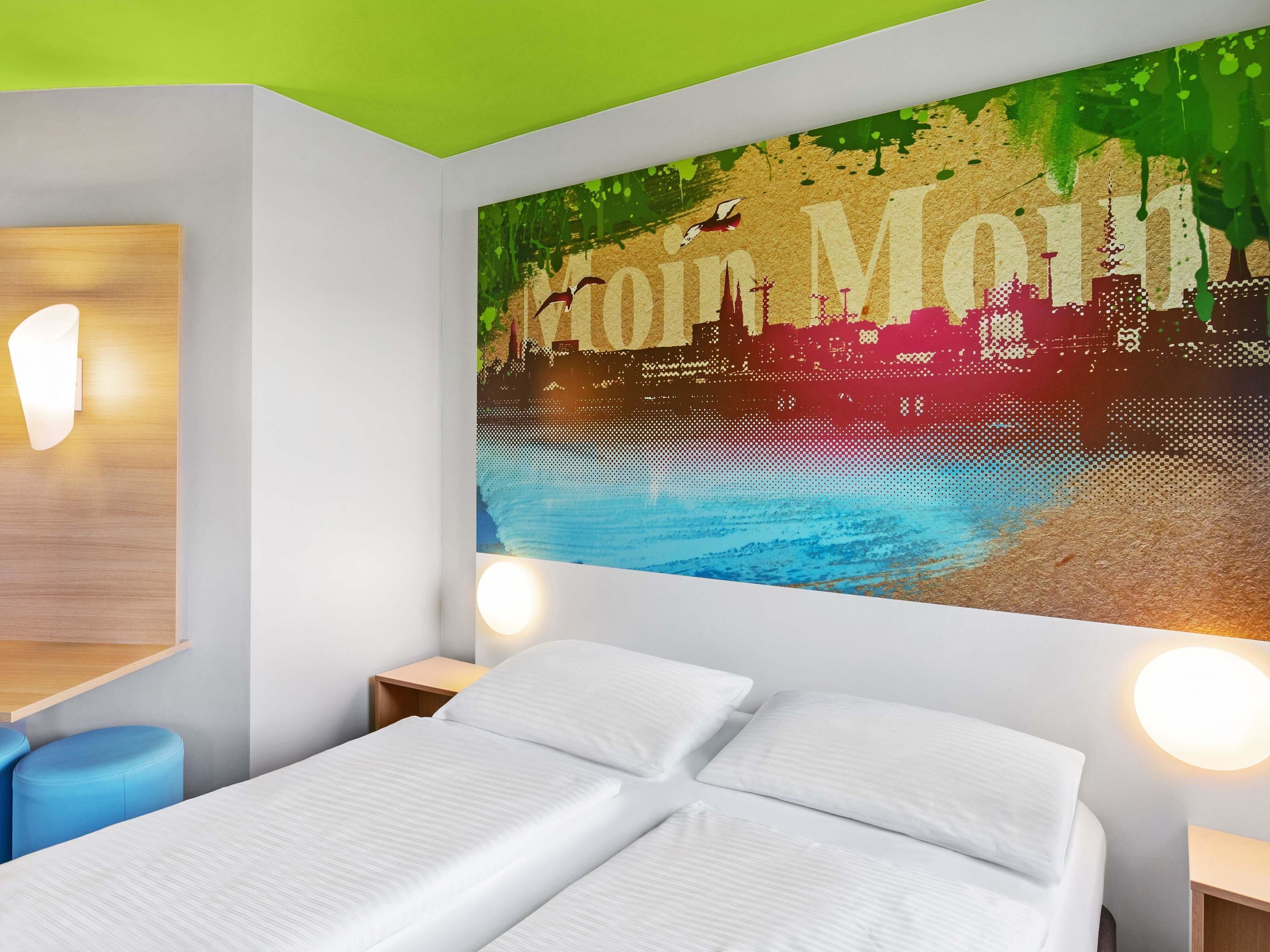 A modern hotel room with a bed, two bedside tables, and a large wall mural.