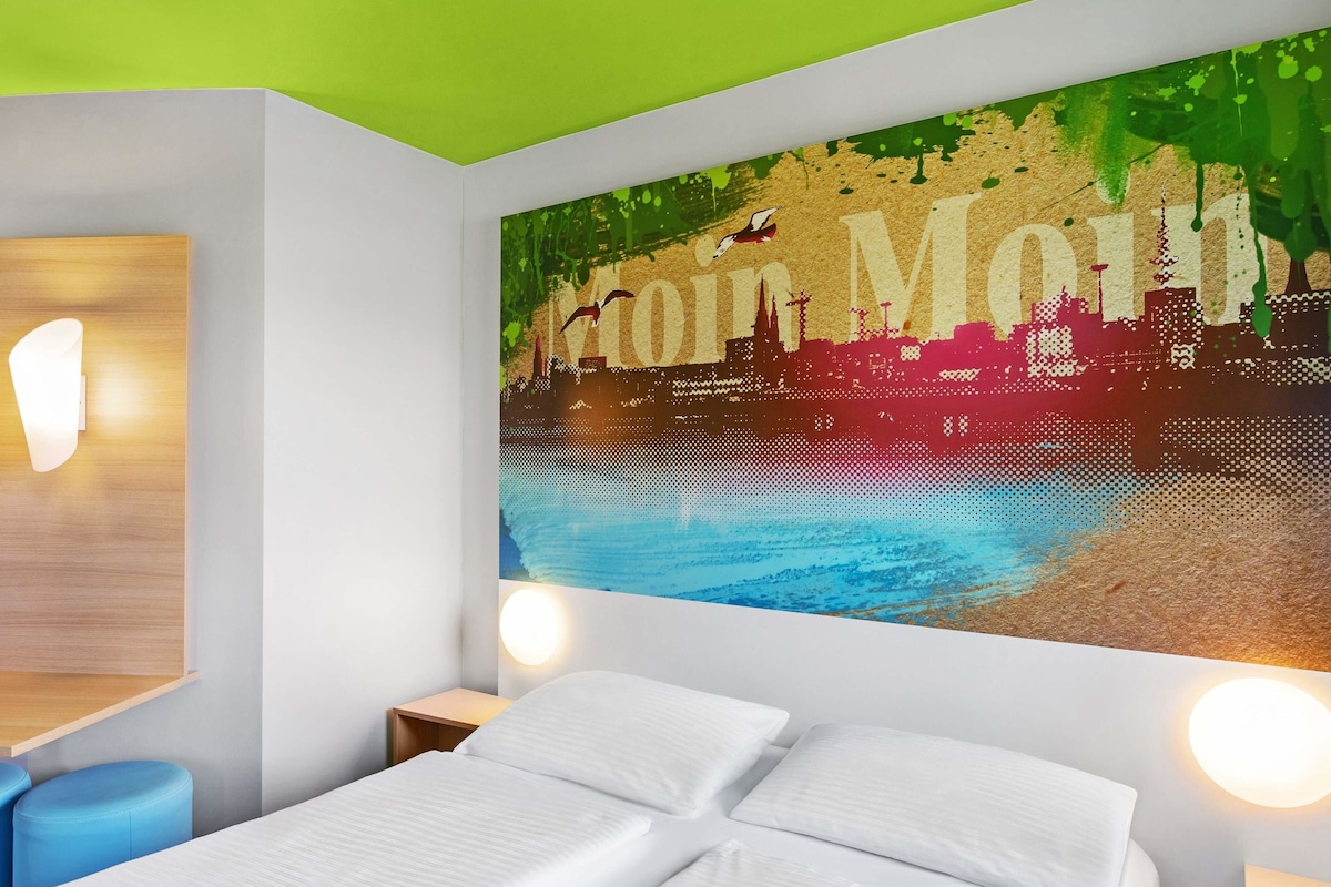 Une chambre d’hôtel moderne avec un lit, deux tables de chevet et une grande fresque murale.