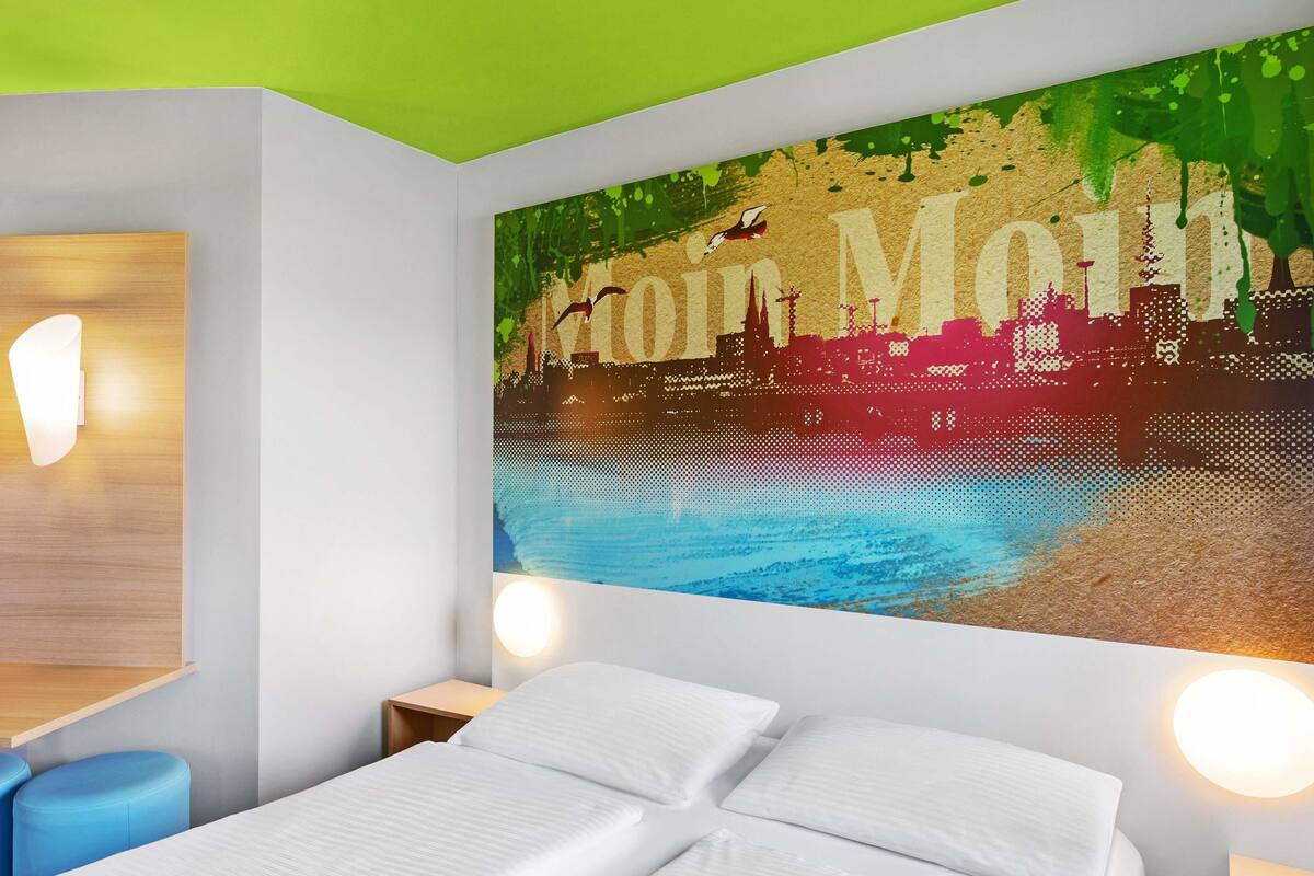 A modern hotel room with a bed, two bedside tables, and a large wall mural.