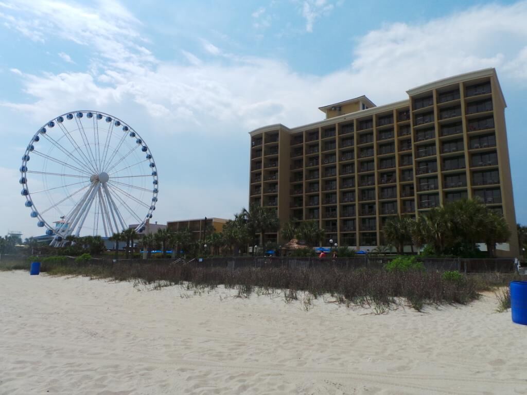 Un hotel frente a la playa con una noria al fondo.