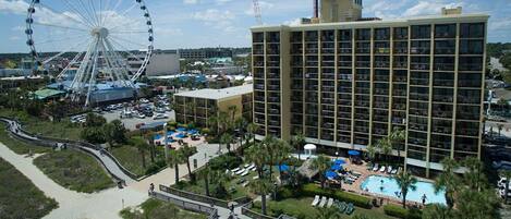 A hotel with a large building, a swimming pool, and a Ferris wheel in the background.