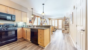 A modern kitchen with wooden cabinets, a black stove, and a stone accent wall. - On Sierra Star Golf Course, Bright Unit, Private Gas Grill, Pool On-site (Mammoth Lakes)