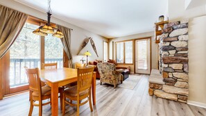 Relax in this inviting living area with a dining table, armchair, and sofa, featuring a cozy fireplace and expansive views.