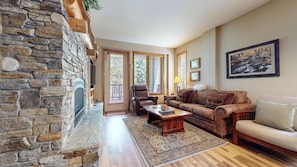A living room with a stone fireplace, a leather armchair, a sofa, and a large painting on the wall. - Pet-Friendly, Steps to Eagle Lodge. Washer/Dryer, 1-Car Garage & Hot Tub (Mammoth Lakes)