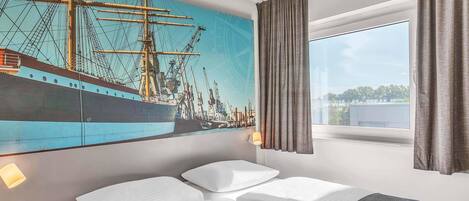 Une chambre d’hôtel avec un grand lit, une table de chevet, une fenêtre avec des rideaux et une fresque murale représentant un navire.