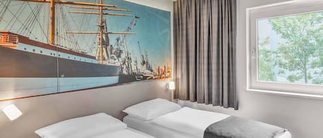 A hotel room with two beds, a large ship painting on the wall, a window with curtains, and a nightstand.