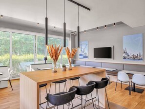A modern kitchen with a wooden island, bar stools, and large windows offering a view of greenery.