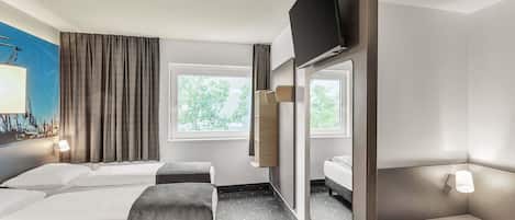 A hotel room with two beds, a desk, a chair, a TV, and a window with a view of trees.
