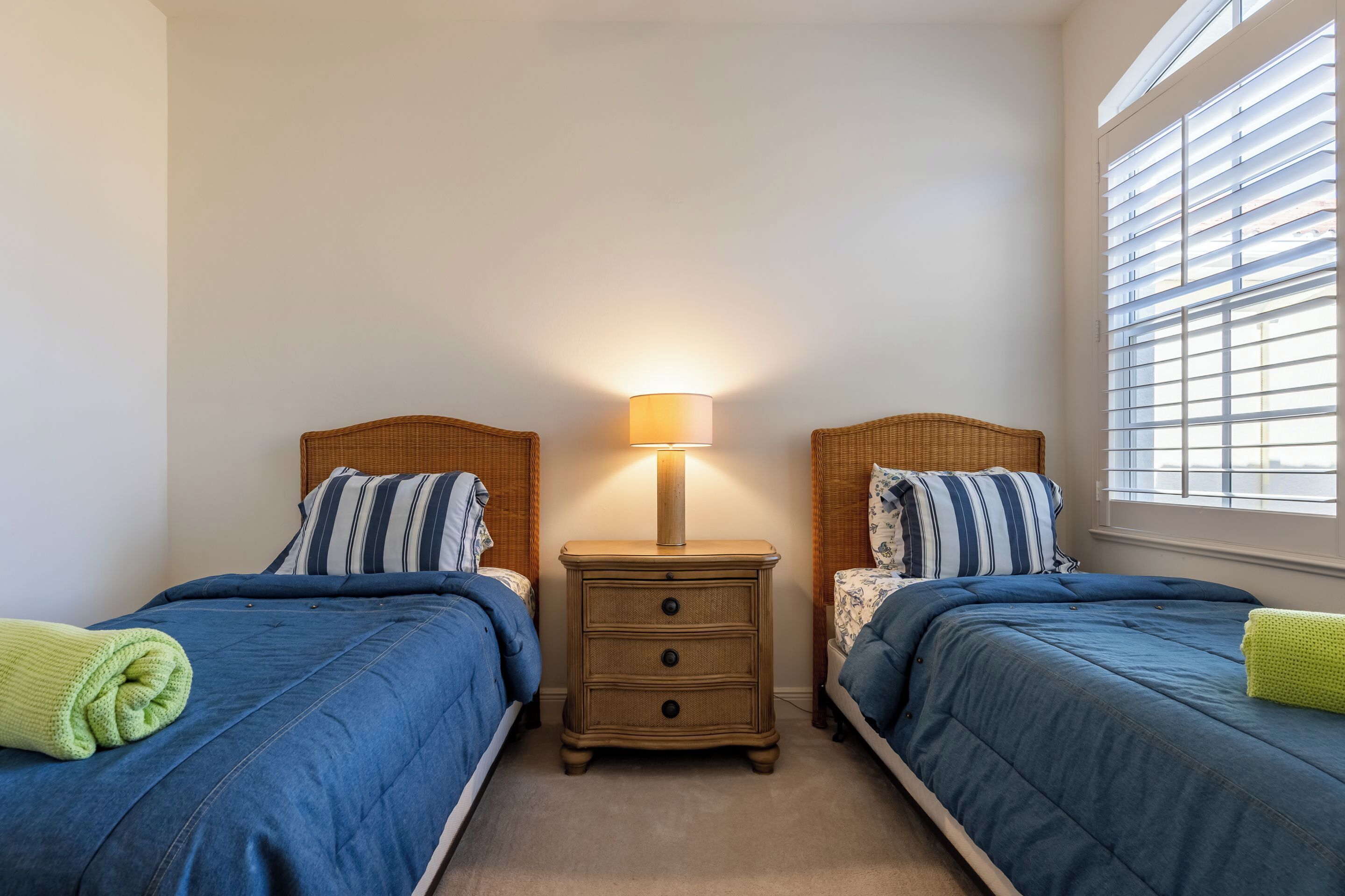 Une chambre avec deux lits, une table de chevet avec une lampe et une fenêtre avec des stores.