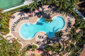 Oversigtsbillede af et resort med en stor swimmingpool omgivet af palmer og liggestole.