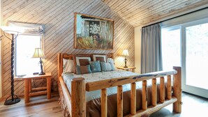A wooden-paneled bedroom with a bed, two bedside tables, a lamp, and a large window.