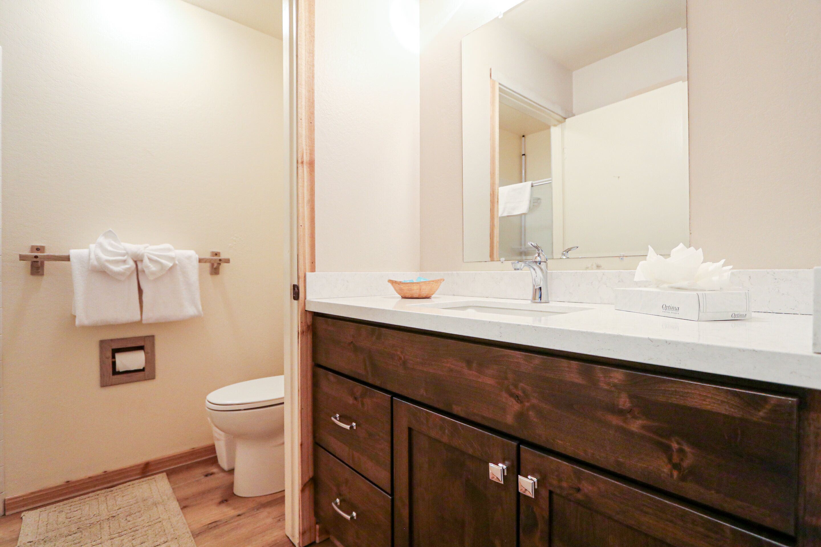 Un bagno con un mobile bagno in legno, un water bianco, un porta asciugamani con asciugamani e uno specchio sopra il lavabo.