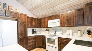 A kitchen with wooden cabinets, a white refrigerator, a microwave, a stove, and a sink.