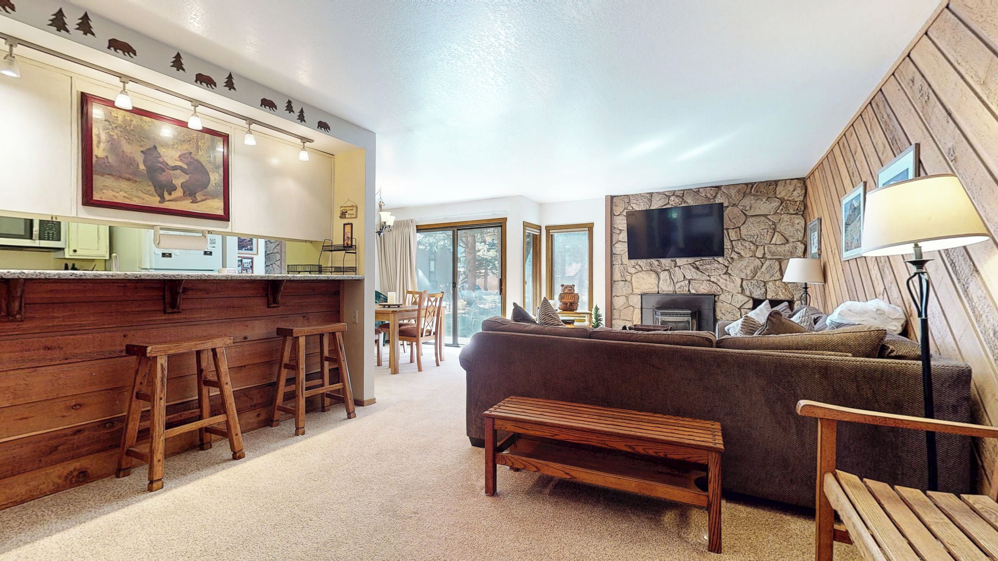 A cozy living room with a fireplace, a stone wall, and a television mounted above it. There is a wooden bench and a sofa in the room.
